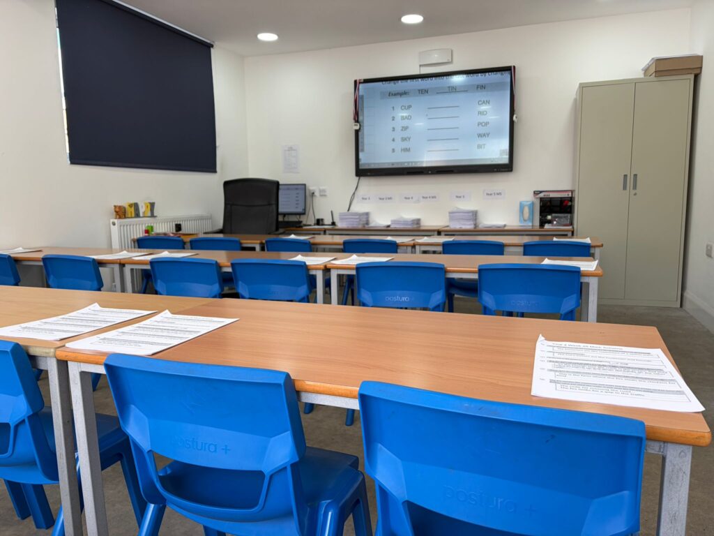 Inside the Pedagogy Club classroom at Avanti Court — desks laid with worksheets, blue chairs, a smart board showing an English exercise