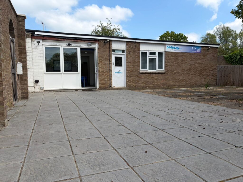 The Pedagogy Club Lodge classroom at Avanti Court — bright room with blue chairs, laminated desks laid with worksheets, a smart board ready for the lesson